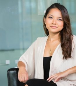 A professional Asian businesswoman sitting confidently in a modern office setting.